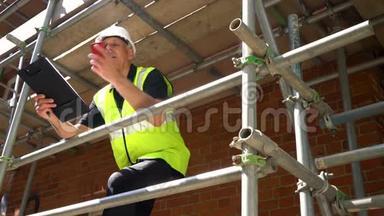 男建筑工领班建筑工人在建筑工地上戴着安全帽，用手机交谈